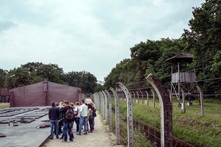 A group of people standing near a barbed wire fence with a watchtower in the background. 4