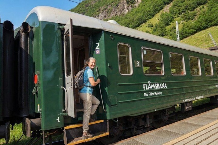 En person stiger om bord på et grønt FLAMSBA tog ved en station. 2