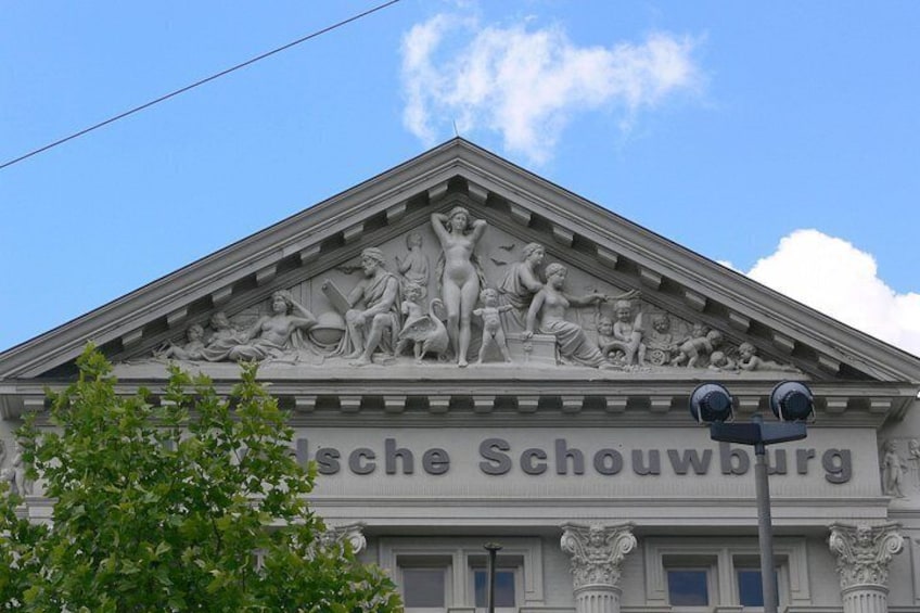 A building with a classical facade, a sculpture of figures, and the name 'Porsche-Schouwburg' on the front. 2
