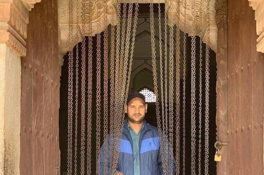 A person standing in front of a wooden door with intricate carvings and chains hanging from the top. 5