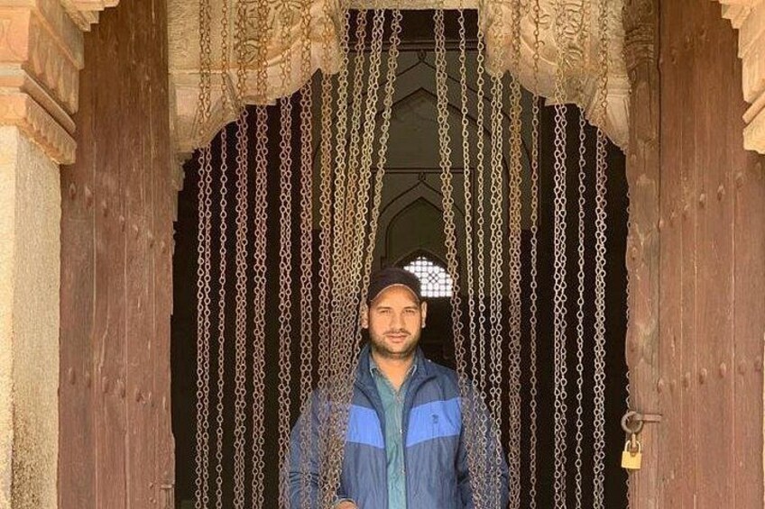 A person standing in front of a wooden door with intricate carvings and chains hanging from the top. 3
