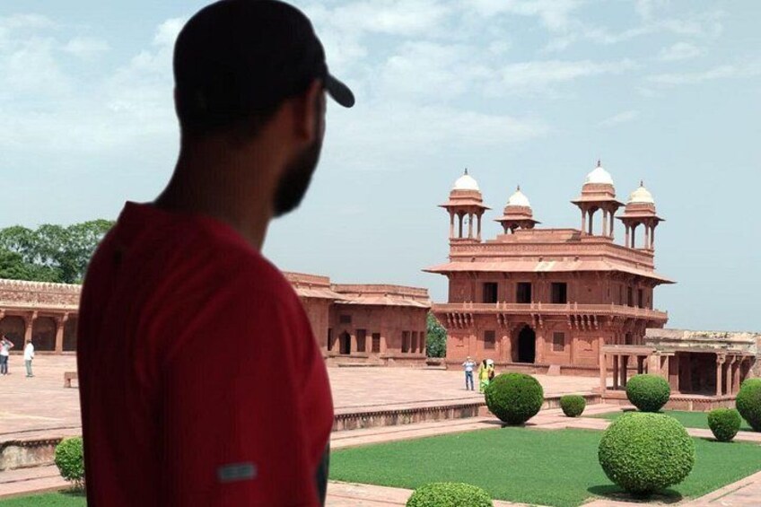 A man in a red shirt standing in front of a large, ornate building with domes and arches. 4