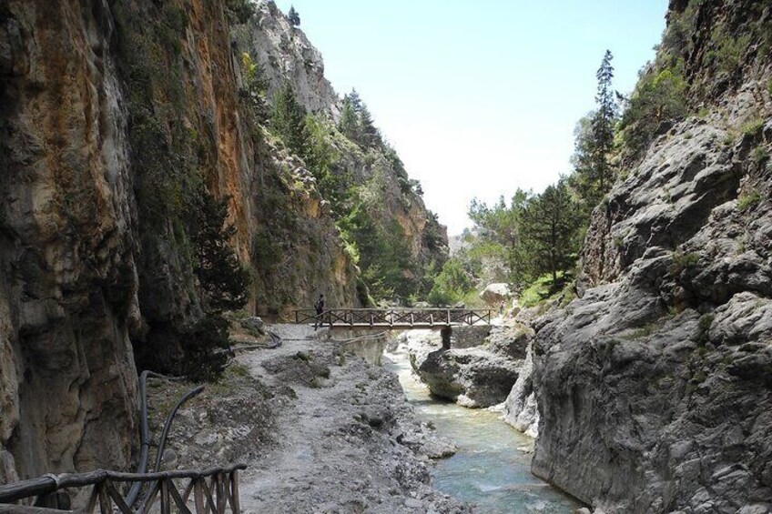A rocky canyon with a wooden bridge over a stream. 1