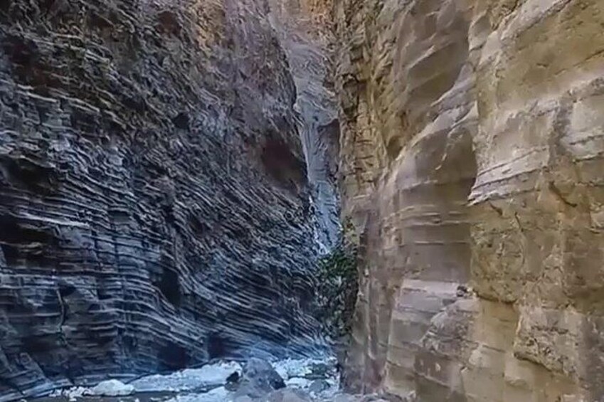 A canyon with layered rock formations and a small stream at the bottom. 4