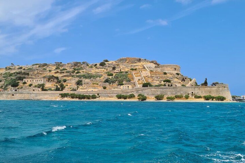 Une ville côtière dotée d’une structure fortifiée perchée sur une colline, d’une mer d’un bleu limpide et d’un paysage rocheux. 1