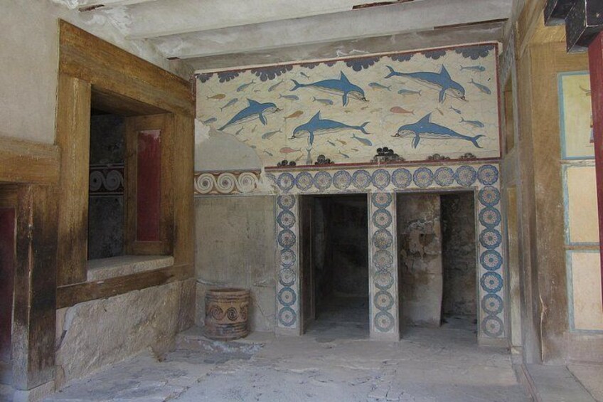 Une pièce ancienne ornée d’une mosaïque représentant des dauphins, avec une porte en bois et une colonne en pierre. 3
