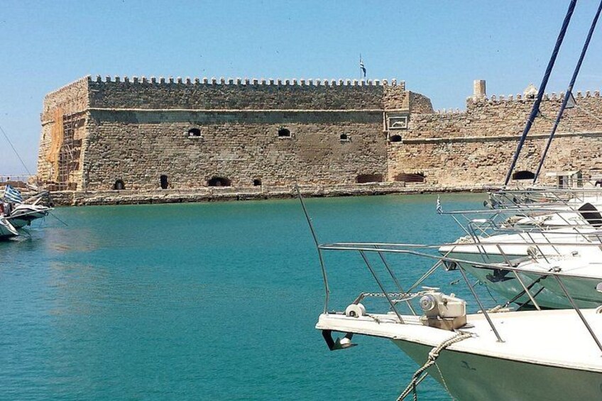 Un bâtiment historique en pierre, situé près d’un port tranquille où sont amarrés des bateaux. 3