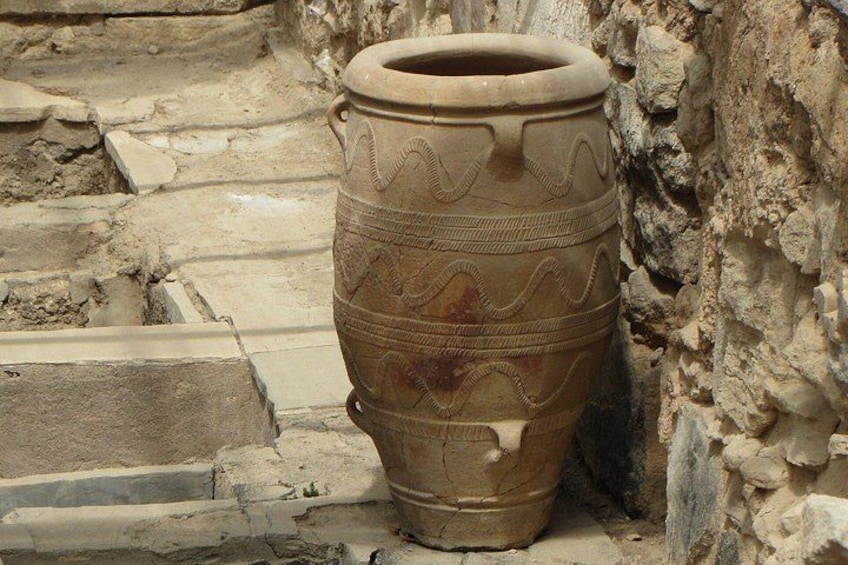 Un ancien pot en terre cuite orné de motifs complexes, posé sur une marche de pierre, à côté d’un mur de pierres brutes. 4