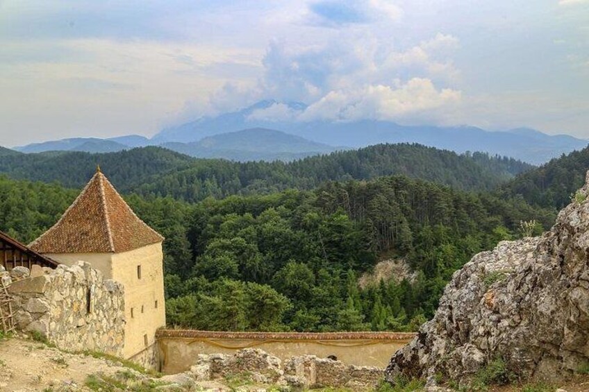 Una torre de piedra, colinas boscosas y montañas a lo lejos. 1
