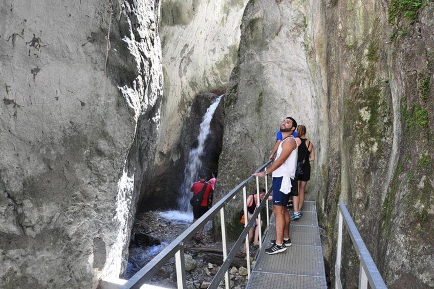 A waterfall cascading down a rocky cliff, a metal walkway with railings, and people observing the scene. 2
