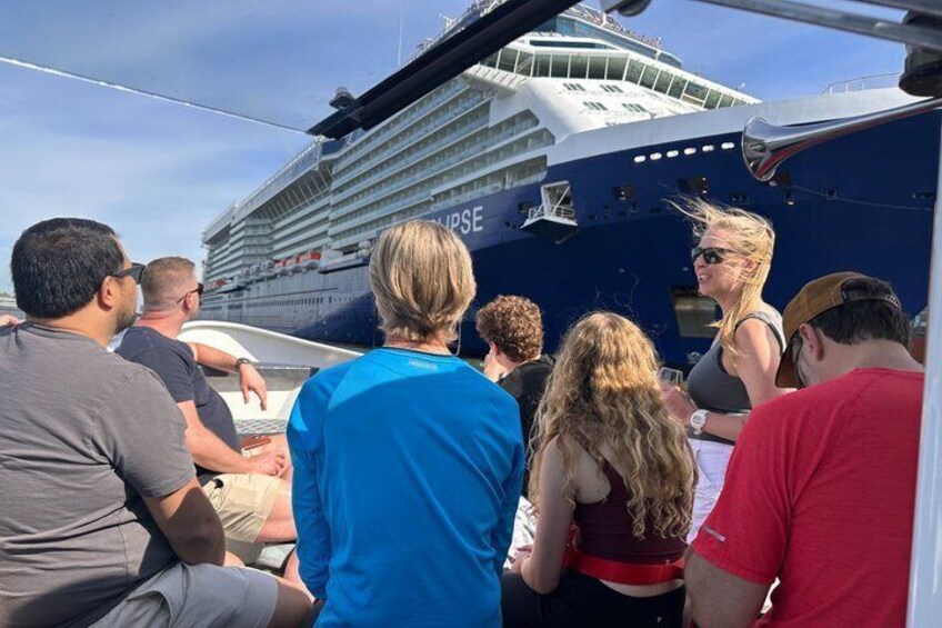 Un groupe de personnes se trouve sur un bateau, avec un grand navire de croisière en arrière-plan. 3