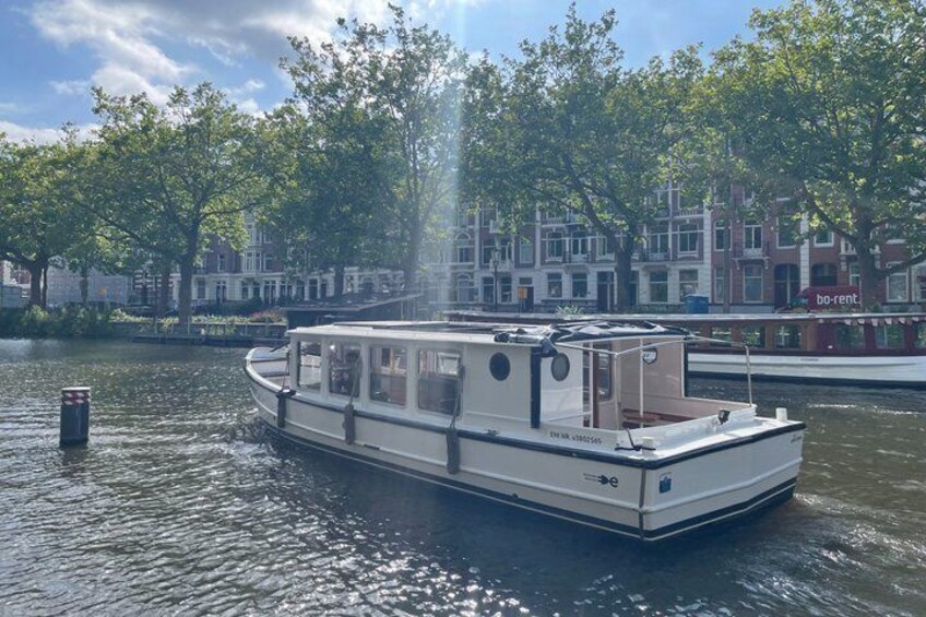 Un bateau de plaisance étroit navigue sur un canal, avec une rangée d’arbres et des bâtiments en arrière-plan. 4
