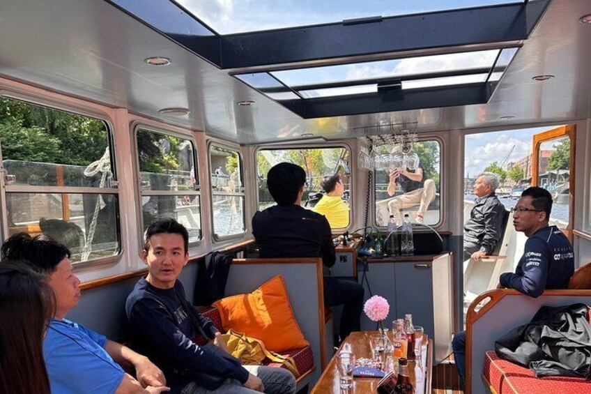 Intérieur d’un bateau avec des passagers assis, un volant et une table sur laquelle se trouvent divers objets. 2