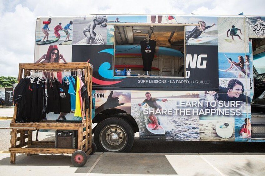 Une publicité pour des cours de surf, affichée sur un camion équipé d’un chariot en bois où sont exposés des vêtements de surf. 2