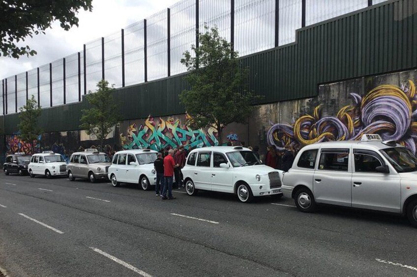 Une rangée de voitures anciennes est garée le long d’une rue, avec une grande fresque murale sur le bâtiment qui se trouve derrière. 2