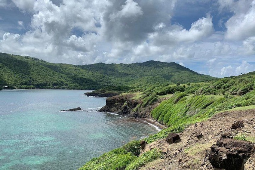 A coastal landscape with a clear blue sea, green hills, and rocky cliffs. 3