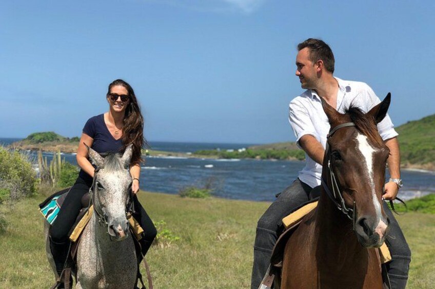Deux personnes à cheval, évoluant dans une zone herbeuse, avec un plan d’eau et des collines en arrière-plan. 2