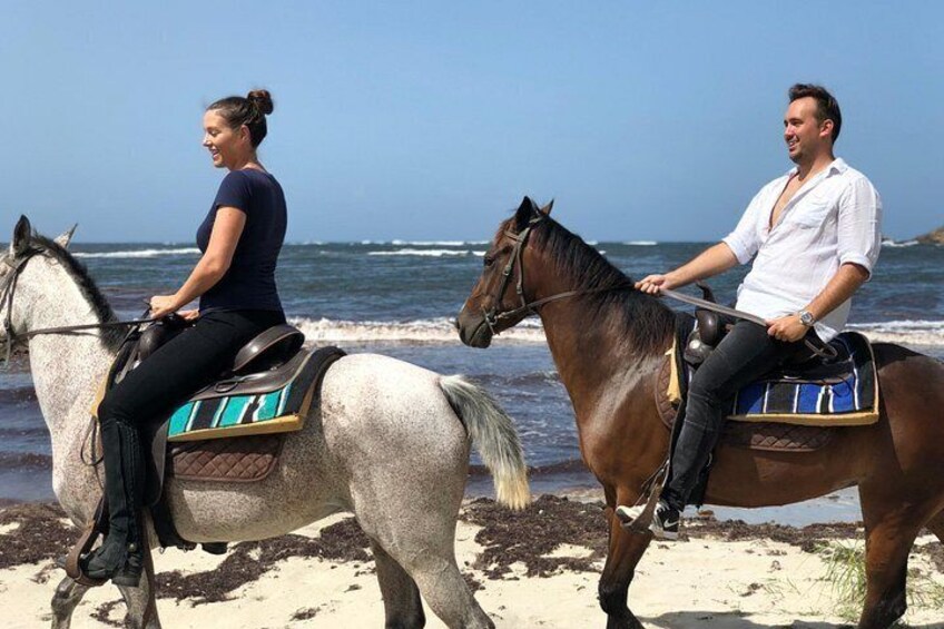 Two people riding horses on a beach with the ocean in the background. 5