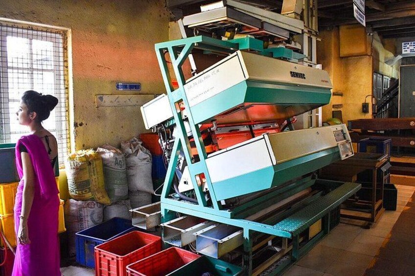 A person in a pink dress standing next to a large industrial machine with multiple compartments, surrounded by storage bins and bags. 2