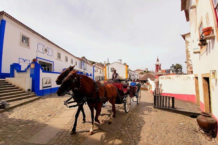 Une rue pavée où circulent des calèches, des bâtiments aux façades bleues et blanches, et un clocher d’église en arrière-plan. 2