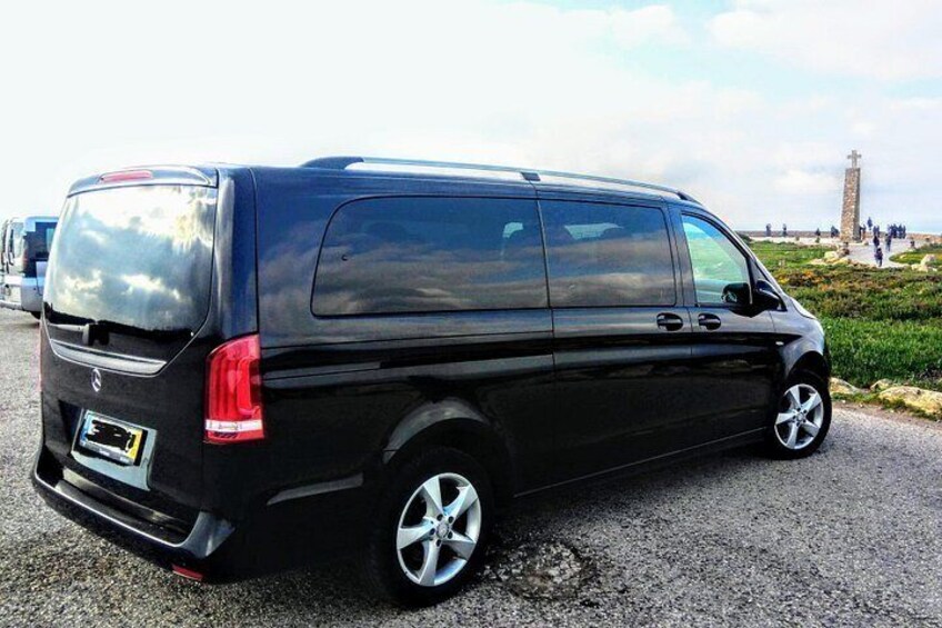 A black van parked on a gravel surface with a cross and a tower in the background. 2