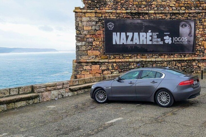 A grey car parked in front of a stone wall with a sign advertising a surfing challenge. 3