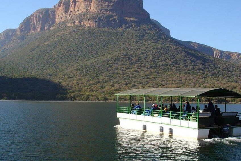 Ein Boot mit Passagieren auf einem ruhigen See, umgeben von üppigen grünen Hügeln und einer markanten Klippe. 1