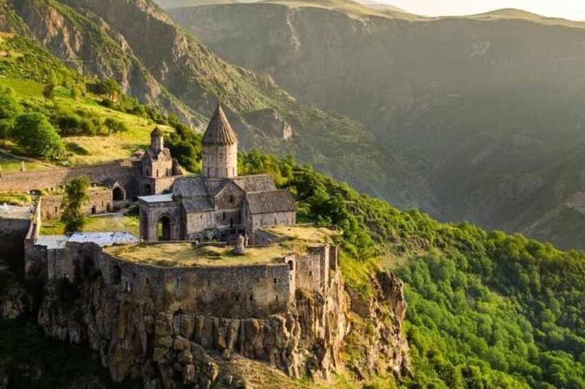 A historic church on a cliffside with lush greenery and mountainous terrain in the background. 2