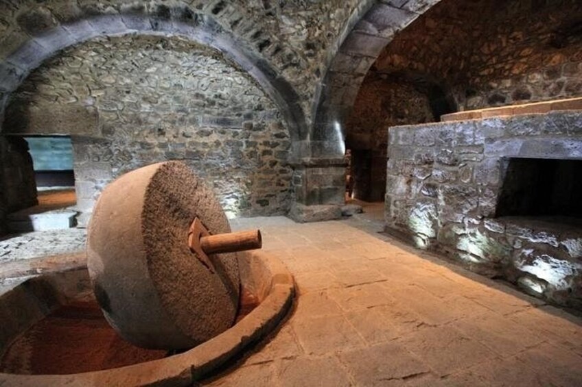 Een stenen watermolen met een groot rad, een gewelfd stenen plafond en een open haard. 2