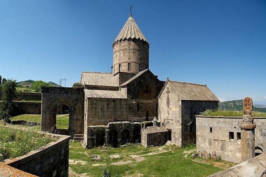En gammal kyrka byggd av sten, med en kupol, omgiven av ruiner och grönska. 2