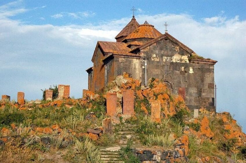 Ein baufälliges Steinhaus mit Ziegeldach, umgeben von überwucherter Vegetation und verstreuten Ruinen. 5
