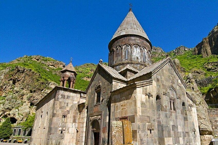 A stone church with a dome and bell tower, set against a mountainous backdrop. 1