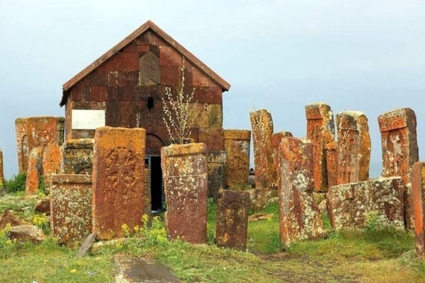 Une structure en pierre délabrée, avec un bâtiment en bois en arrière-plan, le tout entouré de piliers en pierre usés par les intempéries. 4