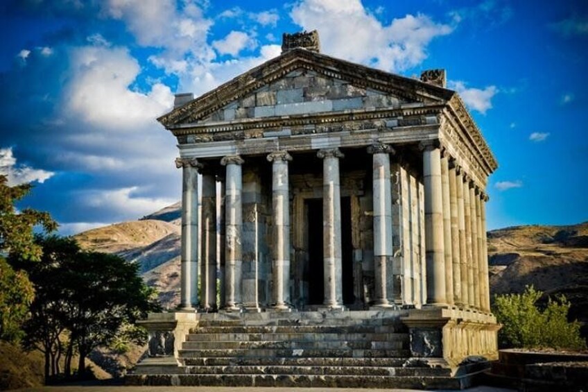A classical building with columns, set against a mountainous backdrop. 3