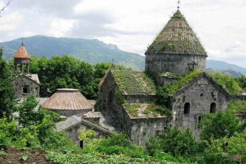 A rural church complex with multiple buildings, surrounded by lush greenery and mountains in the background. 2