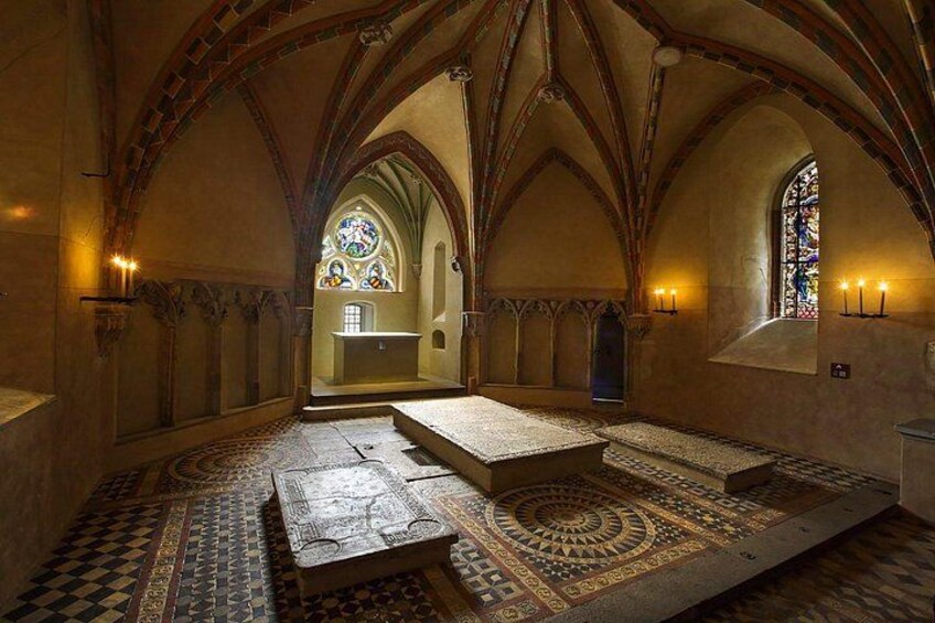 A medieval church interior with arched ceilings, stained glass windows, and patterned floor tiles. 5