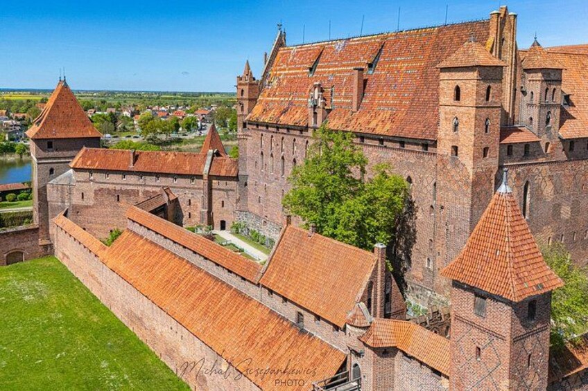 A historic castle with red-tiled roofs, a moat, and a river in the background. 2