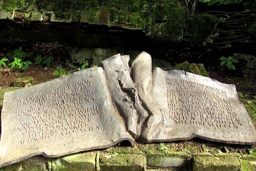 A stone monument with inscriptions, set against a stone wall and surrounded by greenery. 3