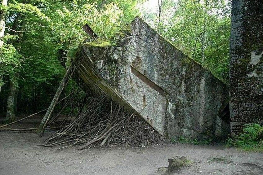 A tilted concrete structure in a forested area with a sign on top. 1