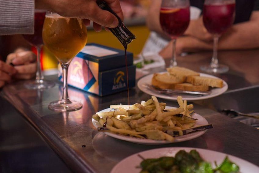 Una persona versa una bevanda in un bicchiere, un piatto di patatine fritte e una scatola di birra Aquila su un tavolo. 3