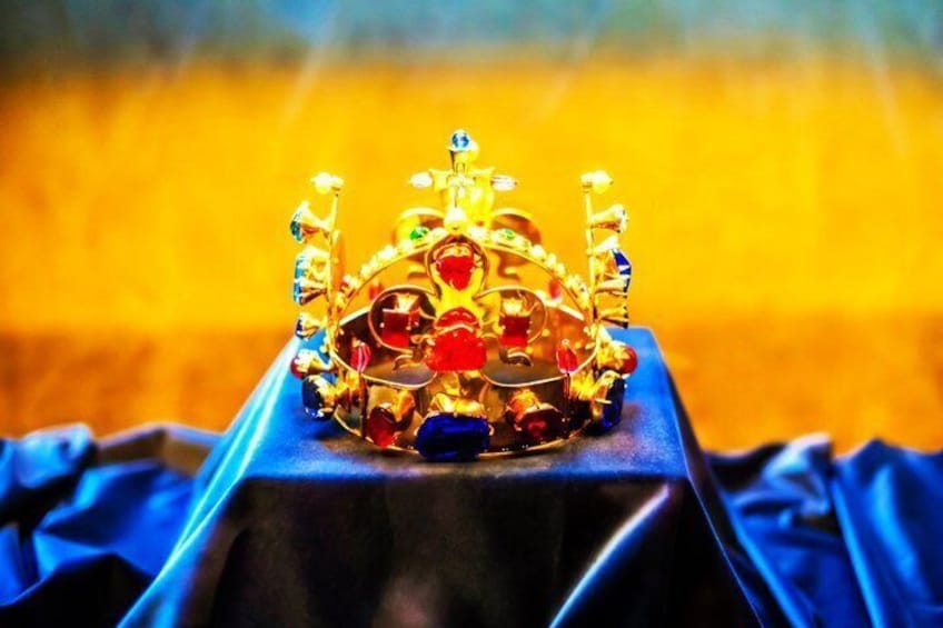 A golden crown with red and blue jewels on a black stand. 3