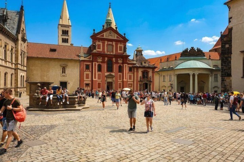 A cobblestone square with historic buildings, a church, and a crowd of people. 3
