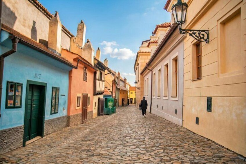 A cobblestone street lined with colorful buildings, a person walking, and a clear blue sky. 4
