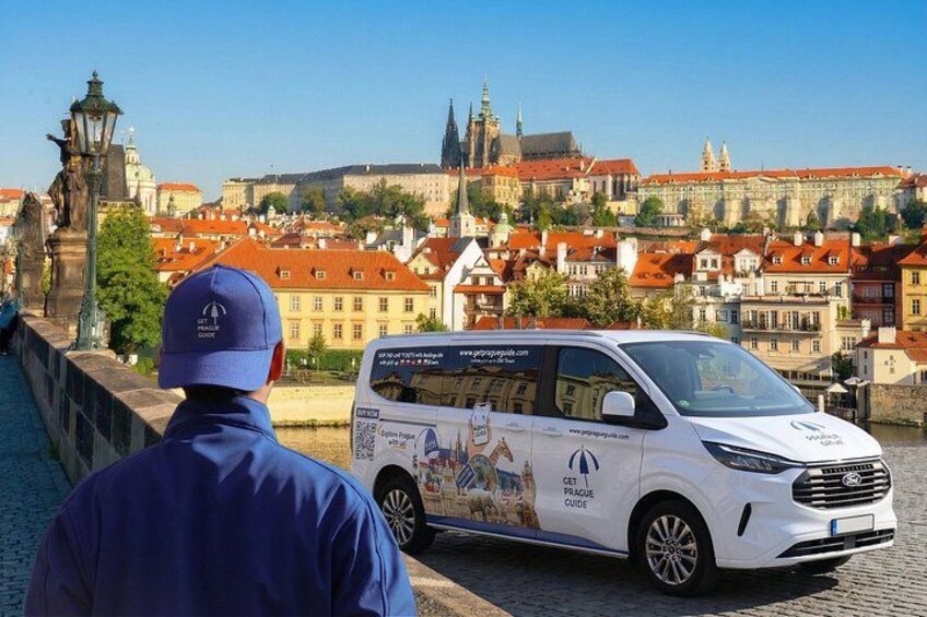 A white van parked on a cobblestone bridge with a cityscape in the background. 1