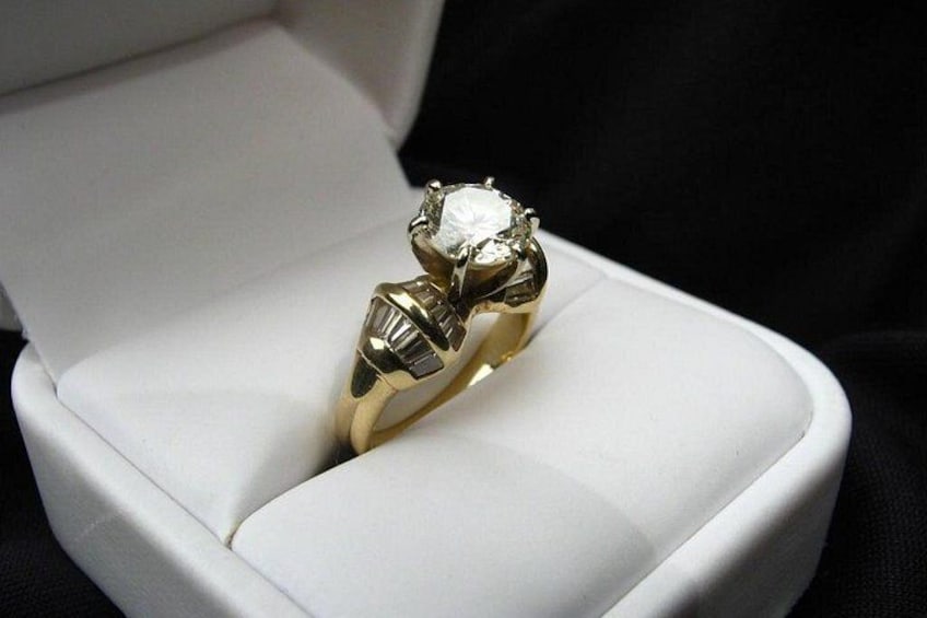 A gold ring with a large diamond in a white box. 2