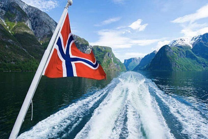 Een boot met een Noorse vlag, een fjord en bergen op de achtergrond. 5