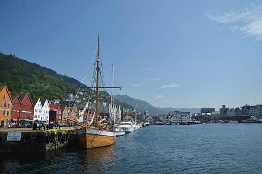 Un puerto con un gran barco de vela amarrado, edificios coloridos a lo largo del muelle y montañas al fondo. 2