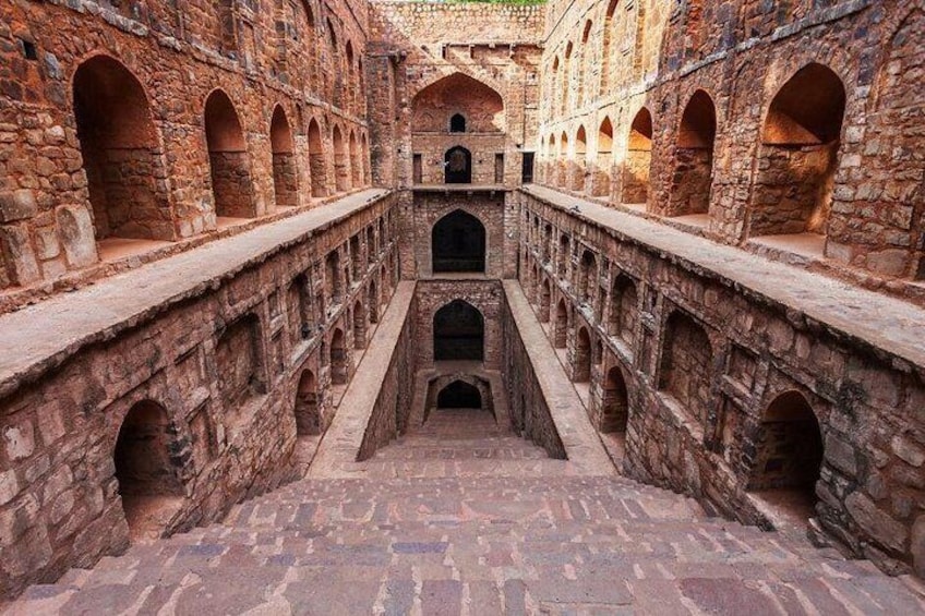 An ancient stone corridor with arched passageways and a central staircase. 2
