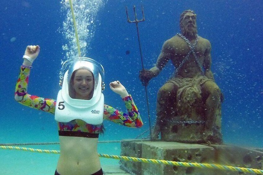 A person in a diving suit with a number 5 on their chest, underwater, with a statue of a figure holding a trident in the background. 3