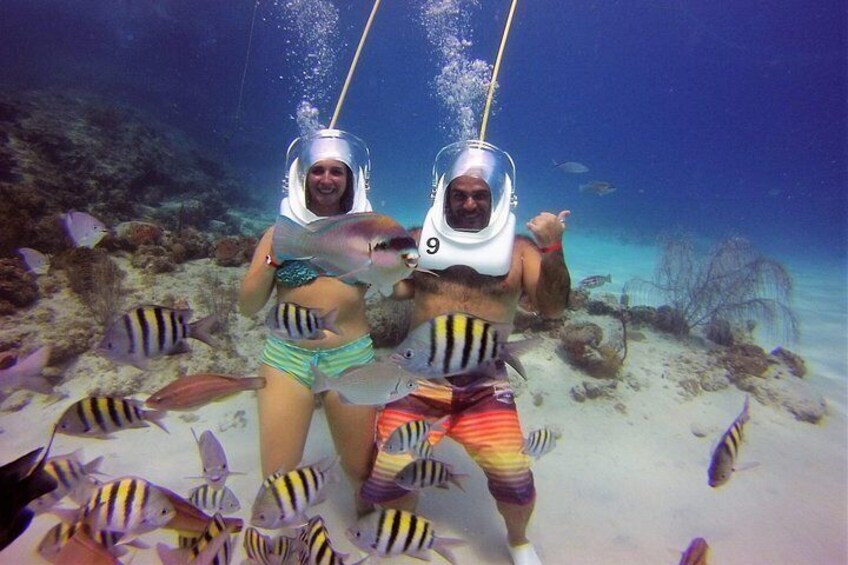 Two people wearing diving helmets underwater surrounded by fish. 5